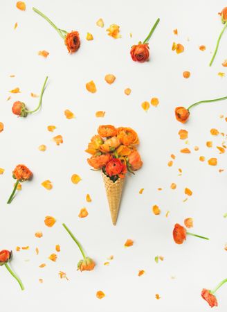 Waffle cone with orange buttercup flowers on a light background, vertical composition