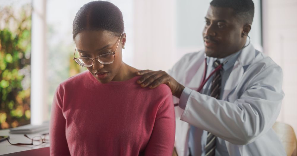 Hospital Ward: Friendly Black Physician Using Stethoscope to Listen to Internal Sounds of Lungs of a Recovering Young Patient
