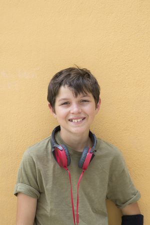 Smiling teen boy posing outdoors with red headphones around neck