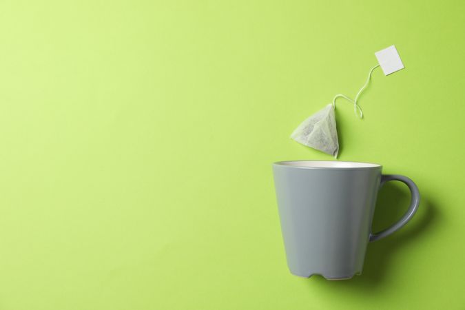 Cup and tea bag on green background, copy space