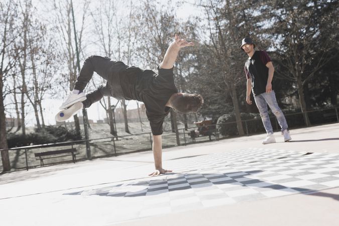 Guy looking at man dancing break dance in park