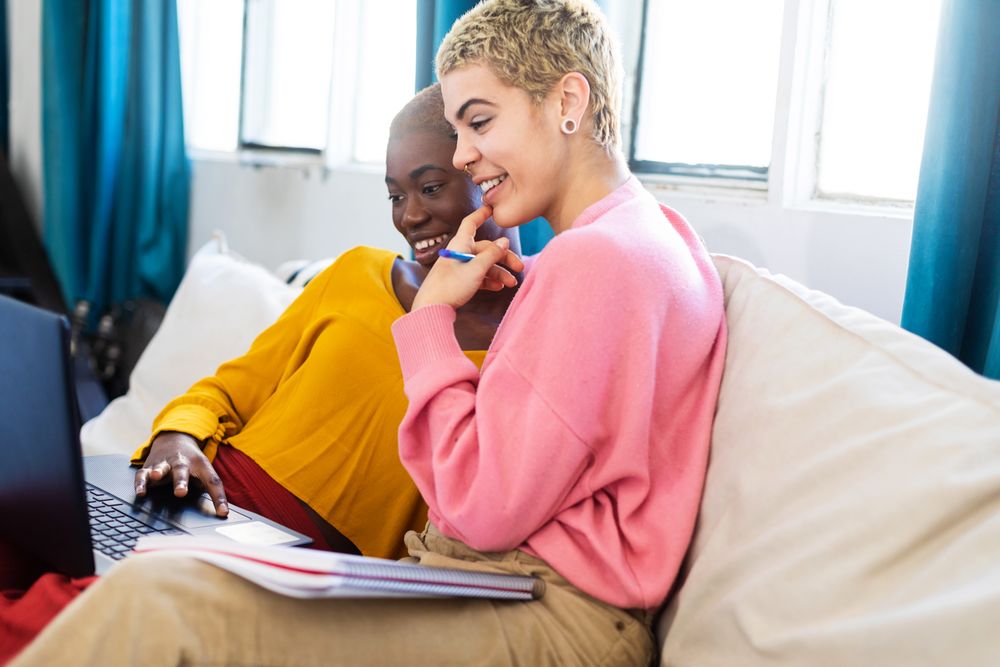 Female couple sitting together on sofa at home with laptop