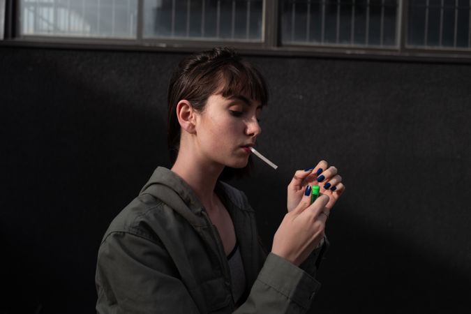 Female teenager in casual clothing smoking cigarette at city street