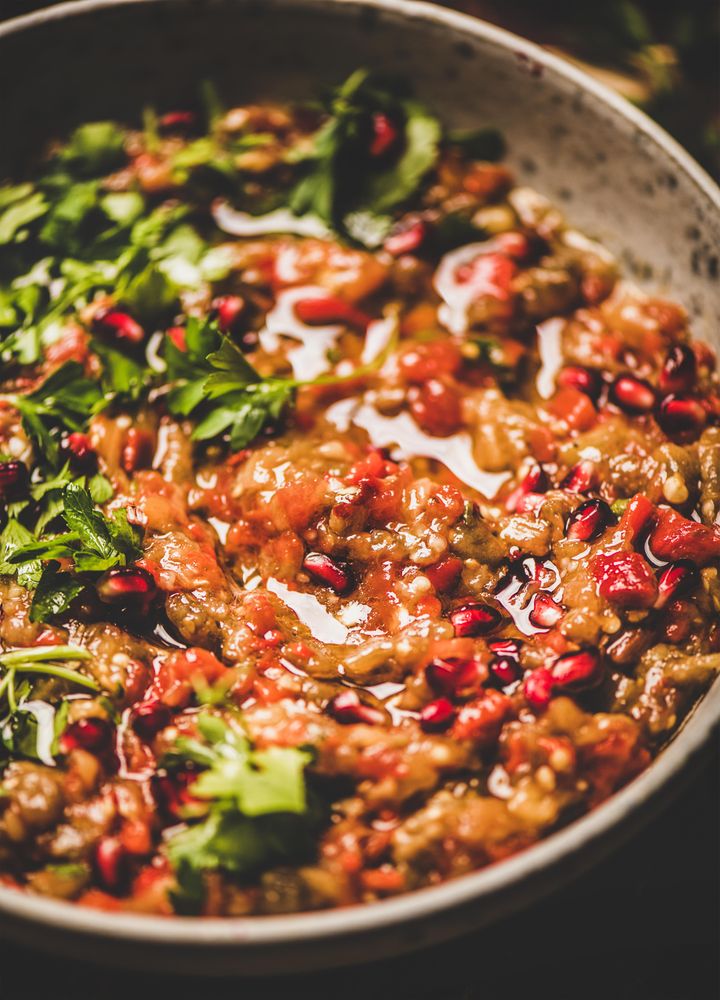 Eggplant dip with pomegranate and parsley garnish on wooden surface, close up