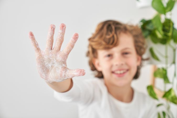 Content boy showing hi gesture with soapy hand