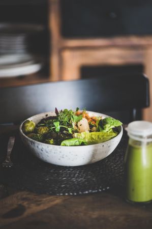 Healthy vegetarian bowl, with smoothie, pictured on table with dark chair, copy space