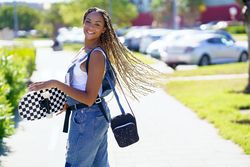 Joyous female in denim overalls holding skateboard and looking around