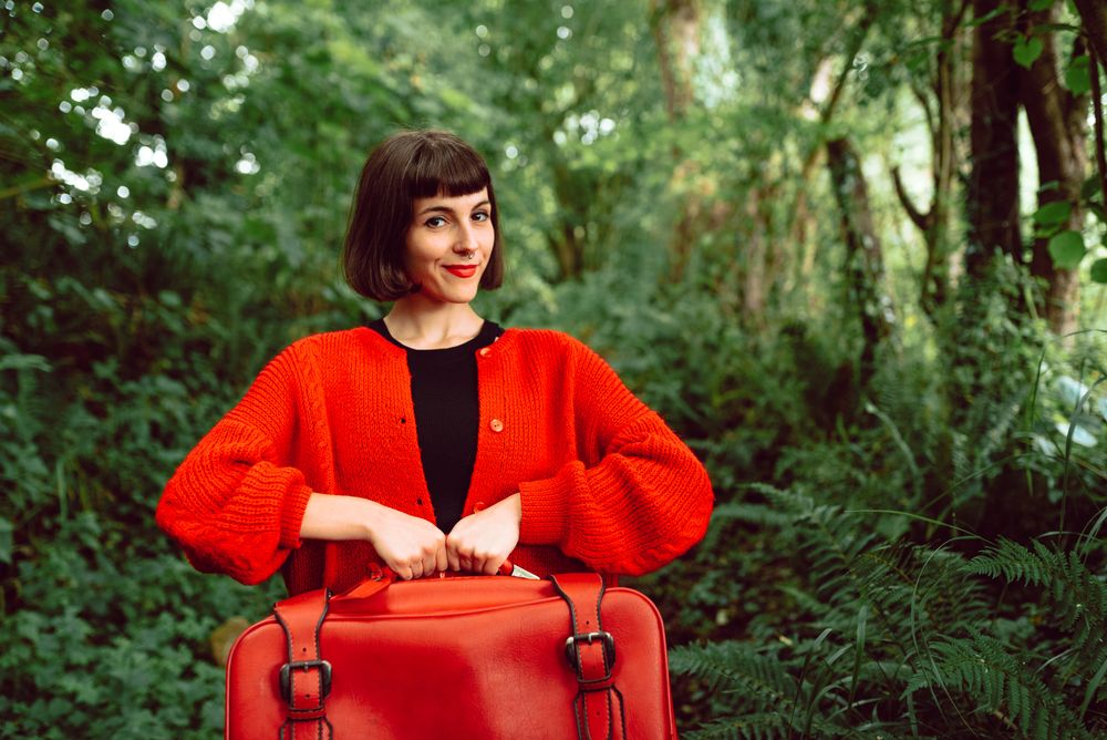 Woman in red with big red suitcase in forest