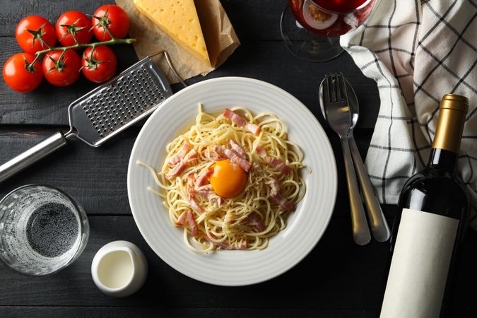 Composition with plate of tasty pasta and ingredients for cooking on wooden background