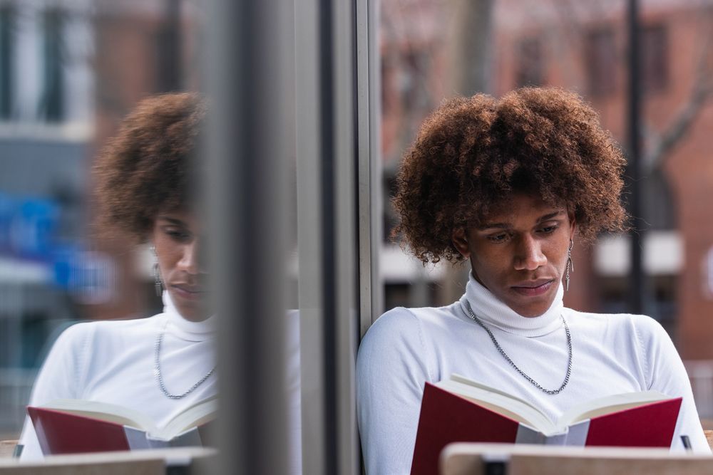 Relaxed young Black man reading book in street cafe