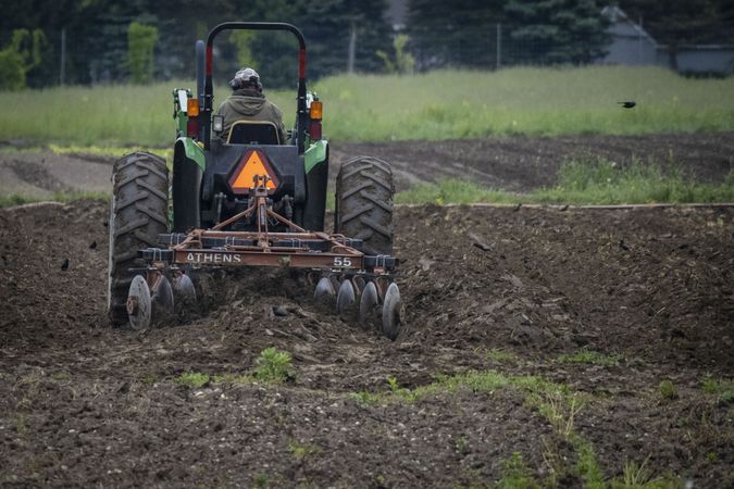 Copake, New York - May 19, 2022: Back of man on tractor in muddy field
