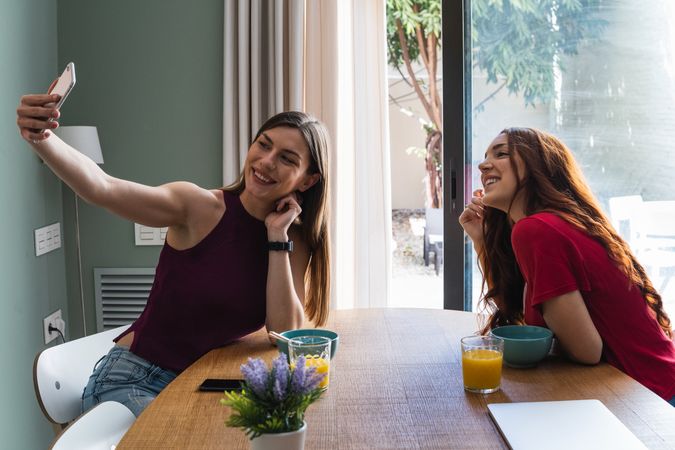 Happy women having lunch and browsing smartphone at home