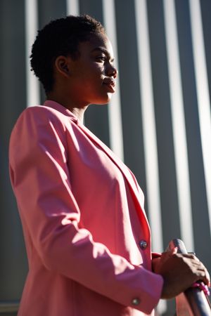 Female wearing suit with pink jacket outside office with striped shadows looking in distance