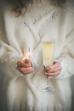 Woman holding crystal flute of champagne and sparkle and sweater