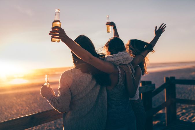 Group of young women enjoying beer at the beach at sunset