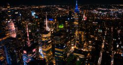 Aerial Shot of Office Buildings at Night. Rooms Have Lights On, Businesspeople and Managers Working Long Hours in New York City. Helicopter Cityscape View of Manhattan in the Evening