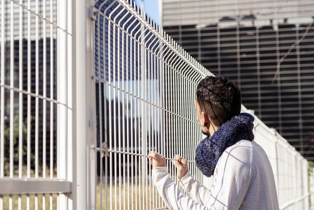 Man leaning on a metallic fence while looking up to the business buildings