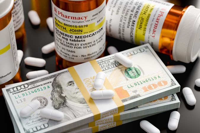 Prescription Medicine Bottles and Pills Next To Stacks of 100 Dollar Bills.