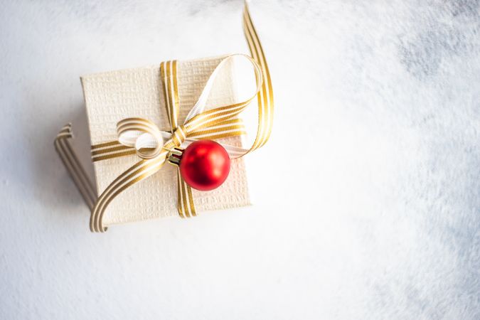 Top view of elegant Christmas present with gold ribbon and red bauble