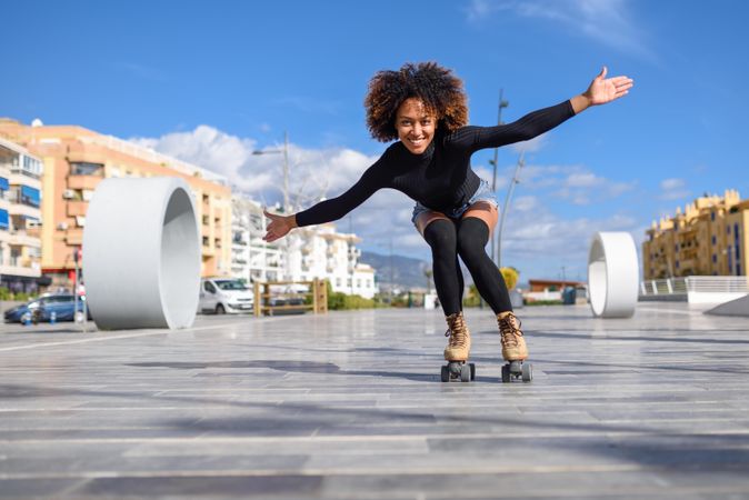 Woman with afro and arms spread roller skating outside