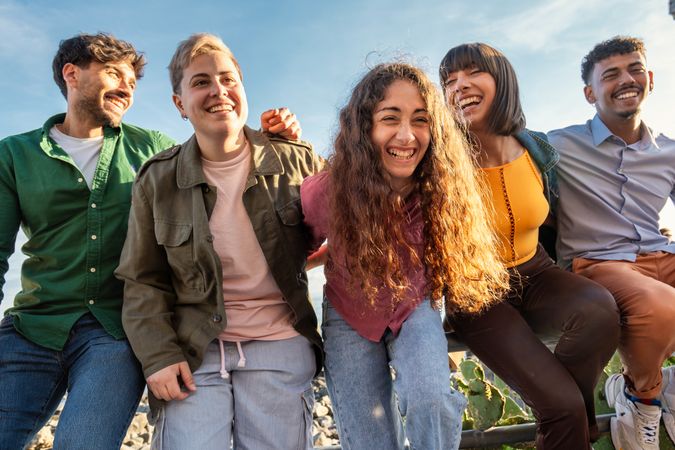 Diverse friends sharing laughter on seaside railing, natural lifestyle portrait