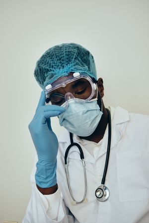Black male doctor in ppe gear with hand to his head thinking