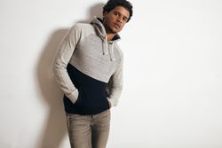 Man with hands in hoodie pocket leaning against wall