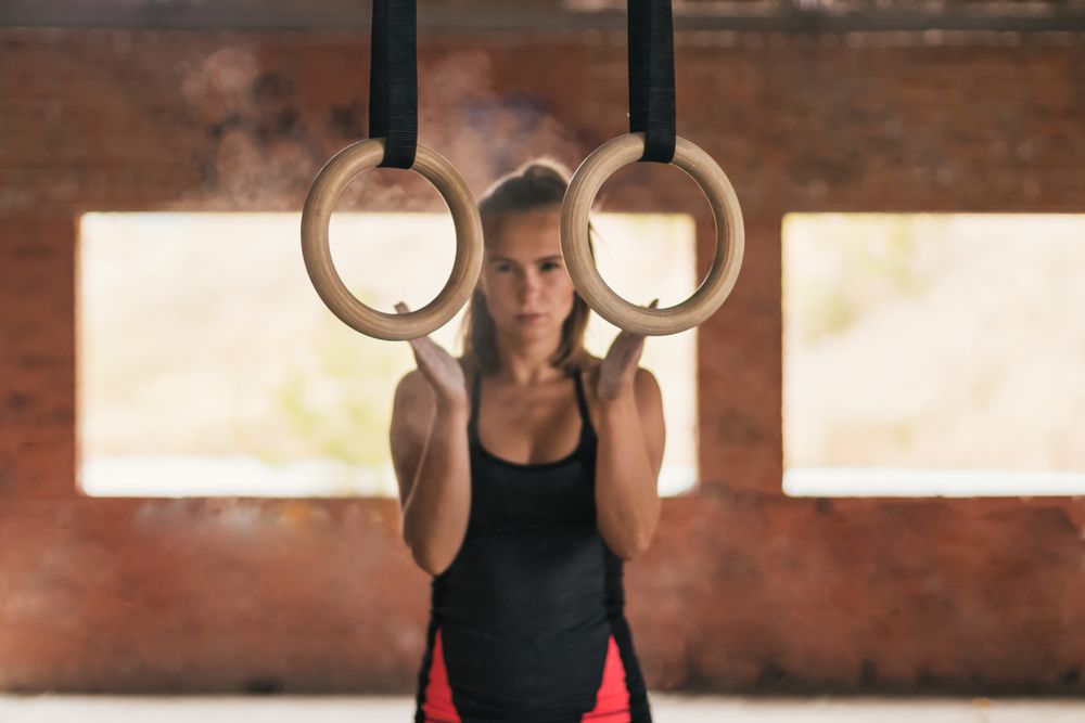 female athlete clapping with chalk in her hands, getting ready to train with gymnastic rings