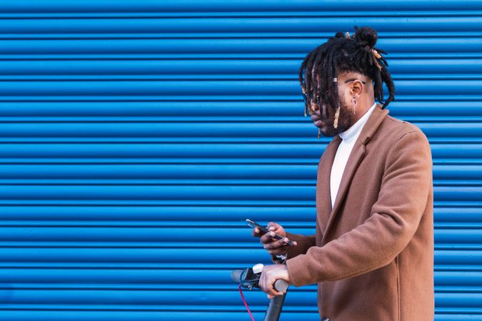 Stylish Black man with electric scooter using smartphone