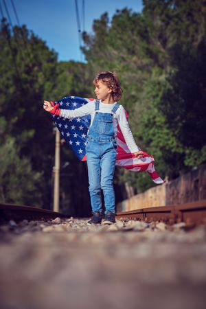 Child standing on railroad with flag of America in summer