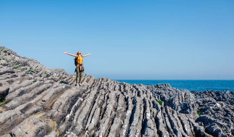 Woman with outstretched arms on rocks near the coast