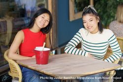 Smiling Asian women in casual clothing sitting together at table in cafe 5wXgJW