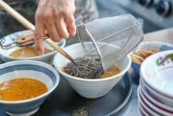 Chef cooking soup with soba noodles in bowl