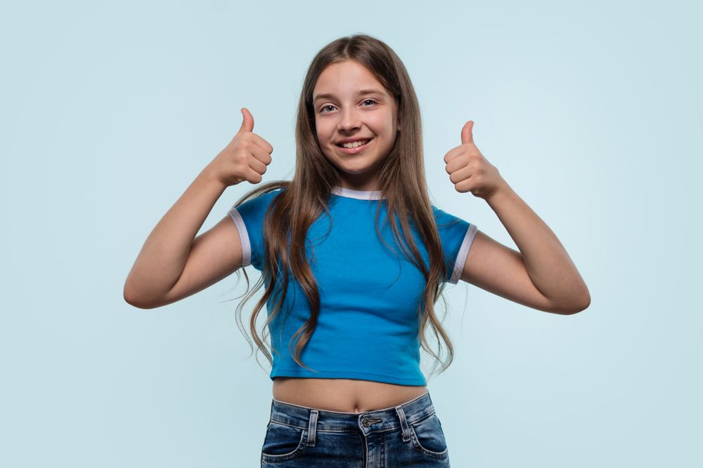 Young girl in blue top confidently gives a thumbs-up.