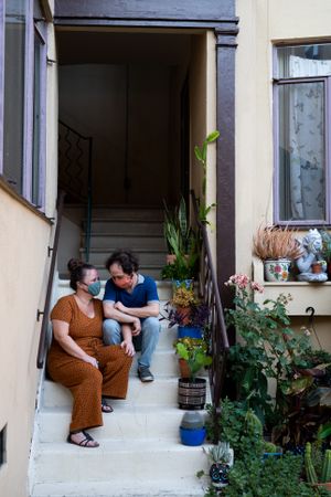 Married couple sitting on stoop with plants wearing coronavirus masks