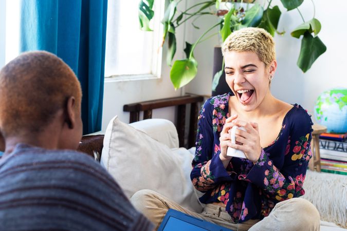 Female couple facing each other and laughing on sofa at home