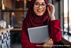 Muslim woman with laptop in hand adjusting her eyeglasses at coffee shop 5pPqv5
