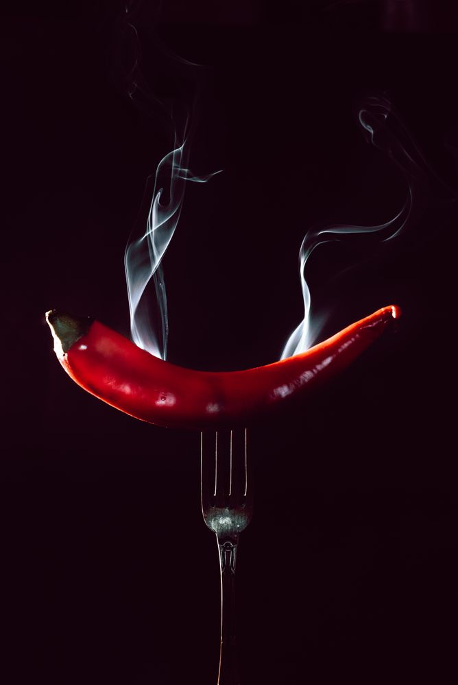 red chili pepper on fire in fork on a dark background
