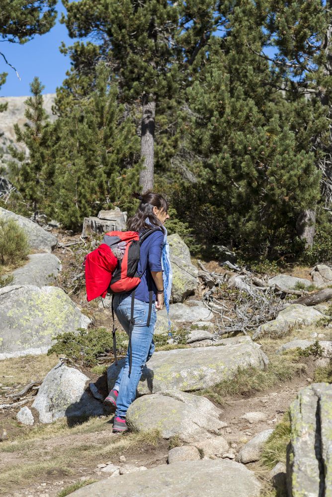 Brunette female trekking in forest in jeans and red backpack