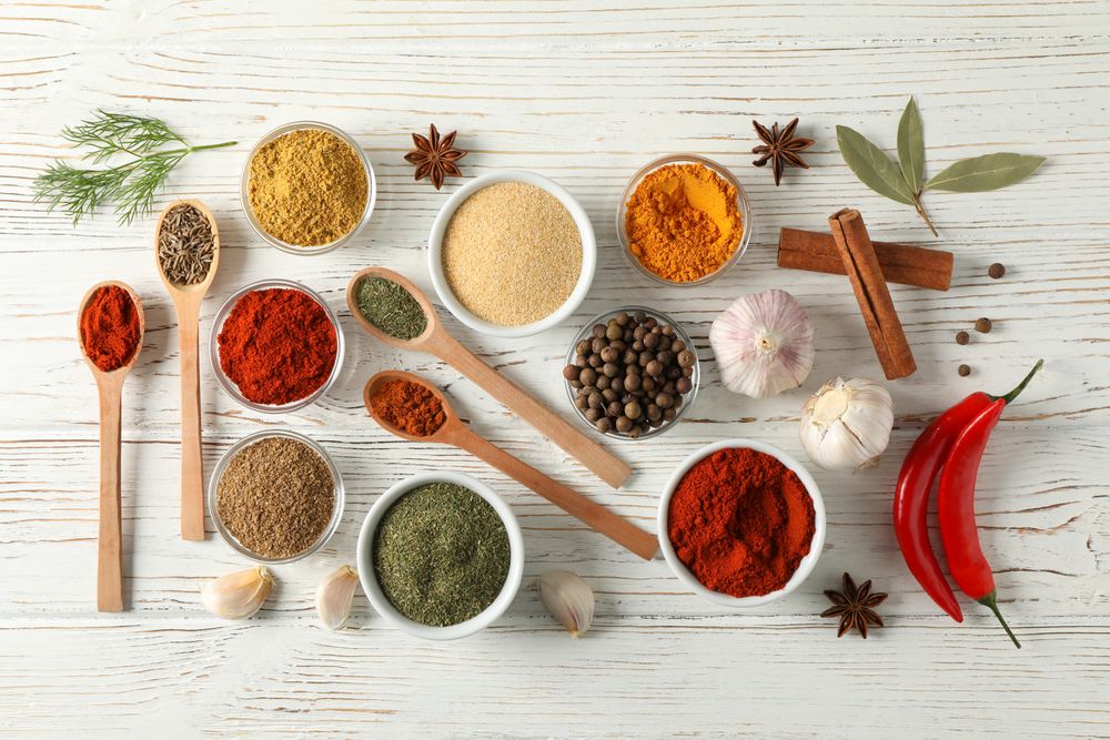 Top view of four wooden scoop full of peppercorn with bowls of spice