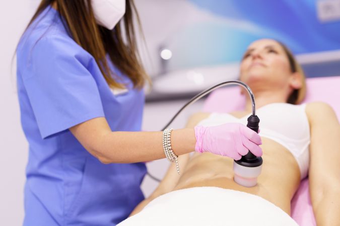 Professional in scrubs performing cosmetic procedure on female’s stomach