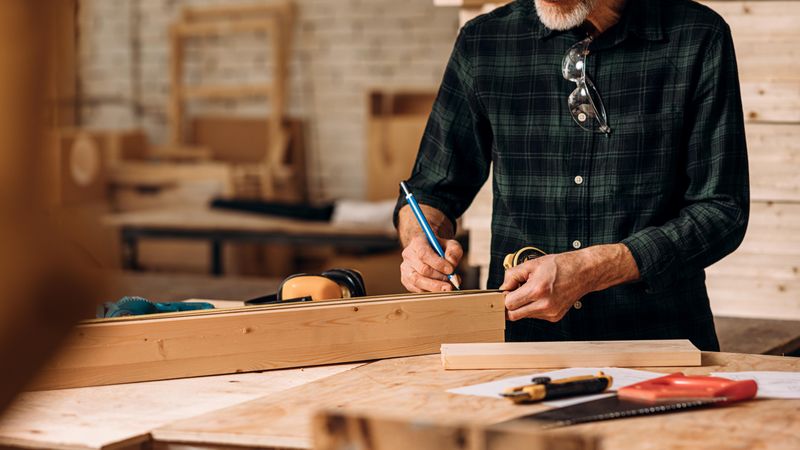 Man marking a piece of wood with pencil to saw in his studio