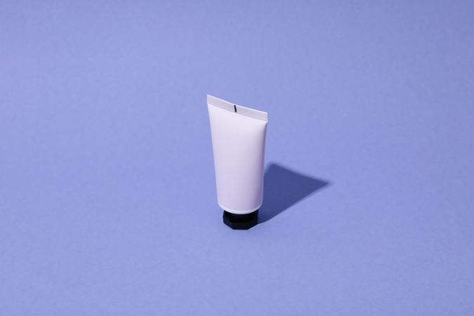 Blank tube of cosmetic on violet background, space for text