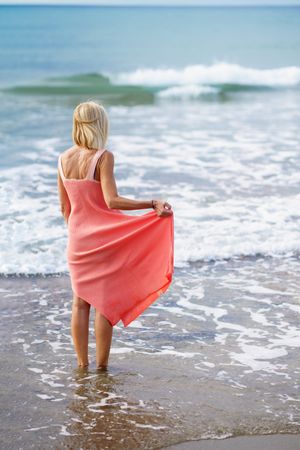 Vertical composition of mature woman standing on the beach facing the ocean