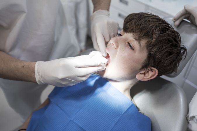 The dentist works on tooth of teenager, vertical
