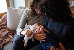 Two women consoling their baby with a toy on the couch