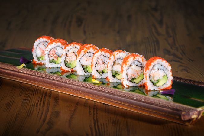 Sushi rolls on serving plank with reflective surface