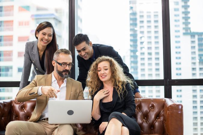 Group of happy businesspeople sitting on couch watching project on computer laptop