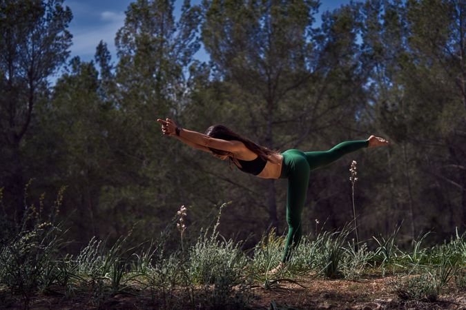 Faceless woman doing Warrior III asana in nature