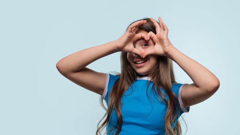 Girl creating heart shape with hands while smiling